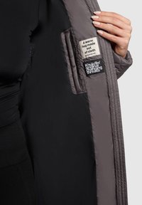 Dark quilted coat with gray lining, featuring multi-fabric pocket labels. The interior showcases a soft texture and structured design.