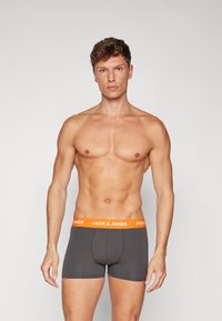 Graue Boxershorts mit einem orangen Bund, der das Logo "JACK & JONES" präsentiert. Der Stoff wirkt glatt mit einem figurnahen Design und minimalen Nähten.