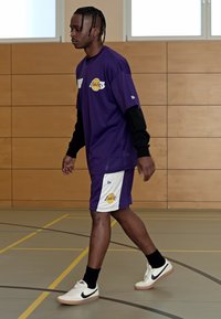 Camiseta de baloncesto morada con acentos negros, pantalones cortos morados a juego con el logo de los Lakers, calcetas negras y zapatillas Nike blancas con suelas rosas.