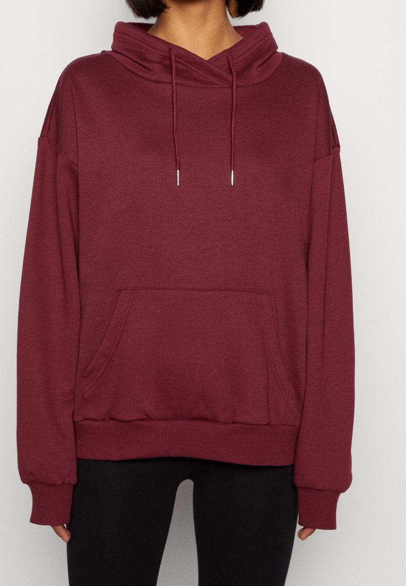 Sudadera con capucha burdeos con cordones, bolsillo tipo canguro, puños acanalados y dobladillo. Textura suave, corte relajado y diseño de hombro caído.