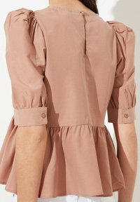 Top peplum in rosa pallido con maniche a sbuffo, busto aderente e polsini bottonati, caratterizzato da un collo rotondo e leggeri raccolti sul retro.