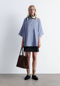 Light purple button-up blouse with wide sleeves, black mini skirt, brown suede tote bag, tan socks, and black slip-on shoes.