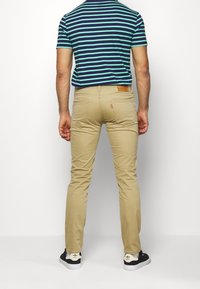 Kaki slim-fit byxor med flera fickor och en läderlogotyp. Bärs med en randig t-shirt i blått och grönt samt svarta sneakers.