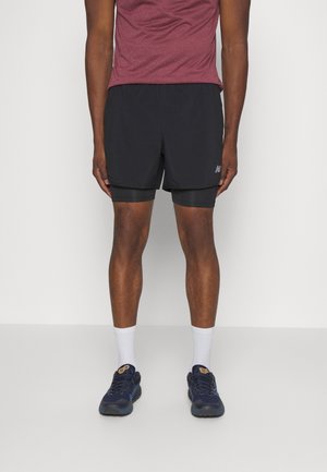 Shorts de sport noirs avec des shorts de compression intégrés en dessous, associés à un t-shirt à manches courtes bordeaux et des chaussures de course bleu marine.