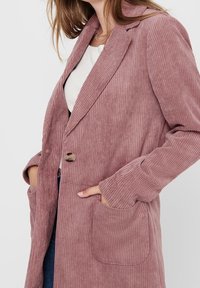 Cordmantel in Staubrosa mit Reverskragen, Einzelknopfverschluss und zwei Vordertaschen. Strukturiertes Gewebe mit vertikalen Rillen.