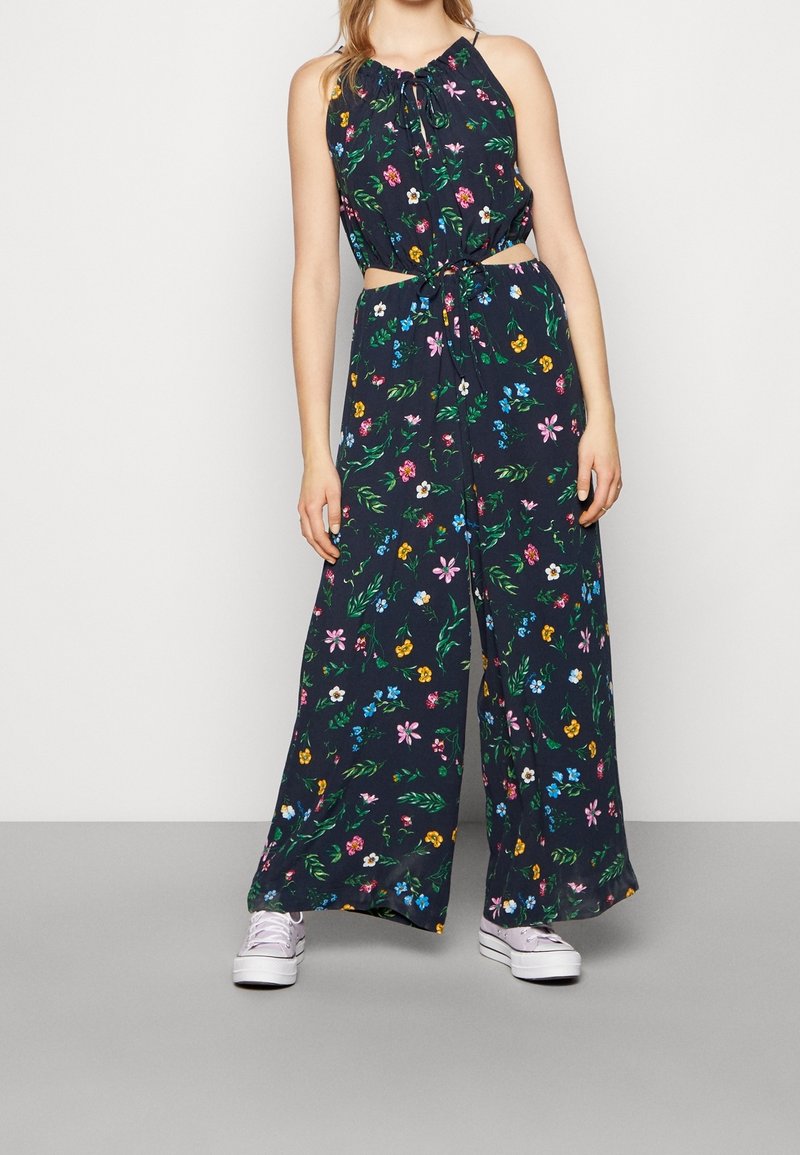 Blommig jumpsuit med marin bakgrund, med halterneck, utskärningar vid midjan och en vid bendesign prydd med olika färgglada blommor.