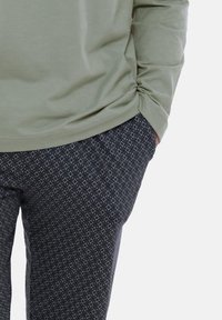 Hellolivgrünes Langarmhemd mit gerafftem Seitendetail, kombiniert mit schwarzen Hosen mit Diamantmuster.