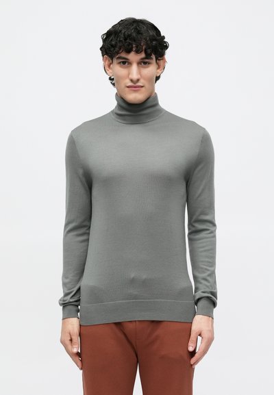 Pull en col roulé gris en matériau doux et léger, avec des manches longues et des poignets ainsi qu'un ourlet côtelés, associé à un pantalon marron.