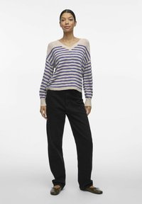 Pull en tricot rayé avec un col en V, présentant des rayures alternées bleues et beiges. Associé à un pantalon large noir et des ballerines.