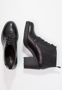 Botas de tobillo de cuero negro con punta redondeada, diseño de cordones y tacón grueso. La suela presenta detalles de agarre texturizado.