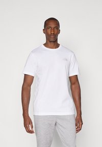 Hvid kortærmet t-shirt lavet af bomuld, med en rund halsudskæring og et lille gråt logo på brystet. Enkel, klassisk design.