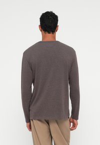 Camicia a maniche lunghe di colore grigio scuro, realizzata in tessuto morbido. Presenta un collo a giro e una vestibilità rilassata, con cuciture minime e senza dettagli visibili.