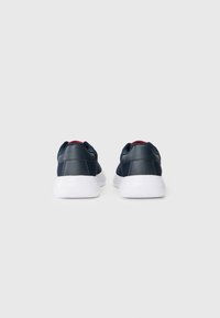 Navy sneakers with textured fabric and smooth leather accents, featuring a white rubber sole and red details around the collar.