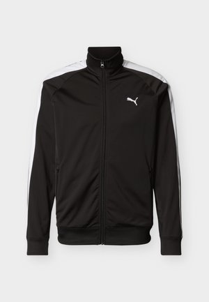 Jachetă neagră cu fermoar, guler înalt, dungi albe pe lateral și manșete elastice. Prezintă un logo pe pieptul superior și buzunare cu fermoar.