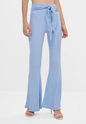 Pantalons en tricot côtelé bleu clair avec une taille à nouer et un bas évasé, présentant une finition texturée et des bords bruts en bas.