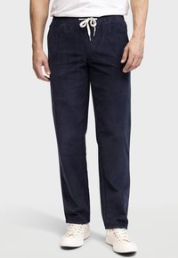 Pantalones de algodón azul marino con cintura elástica, cierre de cordón y un corte relajado. Combinados con zapatillas de color claro.