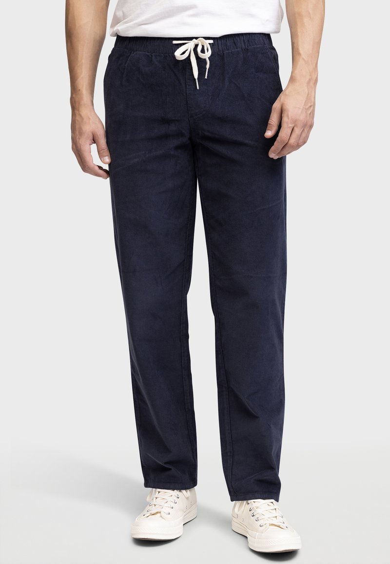 Pantalones de algodón azul marino con cintura elástica, cierre de cordón y un corte relajado. Combinados con zapatillas de color claro.