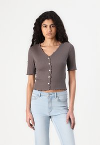 Gray ribbed short-sleeve shirt with a V-neck and scalloped edges, featuring a row of buttons down the front. Paired with light blue jeans.