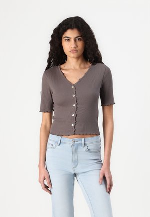 Gray ribbed short-sleeve shirt with a V-neck and scalloped edges, featuring a row of buttons down the front. Paired with light blue jeans.