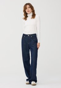 Ciemnoniebieskie szerokie jeansy z wysokim stanem, pięcioma kieszeniami i kontrastowym przeszyciem, zestawione z dopasowaną białą golfem.