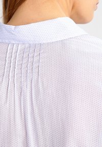 Blouse bleu clair à motifs, dotée d'un col classique, d'un imprimé cœur subtil et de plis à l'arrière, réalisée en tissu doux et léger.