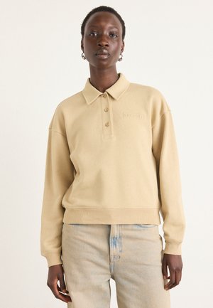 Pullover beige con colletto, tre bottoni e polsini a costine. Presenta un logo in rilievo sul petto e un design dalla vestibilità rilassata.