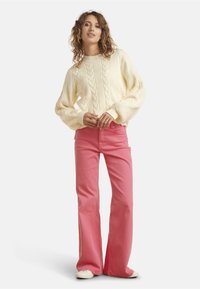 Cream cable-knit sweater with puffed sleeves, paired with pink flared jeans and white sneakers. Simple design, soft texture, and vibrant colors.
