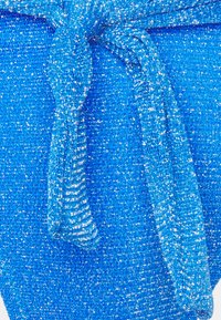 Tecido azul de malha com detalhe em fio metálico. Apresenta um acabamento de nó atado, destacando a textura e o brilho em toda a superfície.