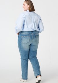 Lichtblauw overhemd met verticale strepen, gecombineerd met aansluitende medium blauwe spijkerbroek. De spijkerbroek heeft achterzakken en een rechte pijp.