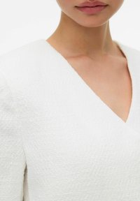 Bíl dresses s texturou, V-výstřihem a strukturovanými rukávy, zdůrazňující jemný vzor a hladký povrch.