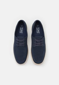 Zapatos de ante azul marino con una textura suave, punta redondeada y costuras en contraste. Cuentan con un cierre con cordones y una suela de goma de color claro.
