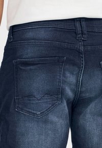 Sötétkék farmernadrág sima textúrával, két hátsó zsebbel és egyenes szárú kialakítással. A varrások jól láthatók a varratok mentén.