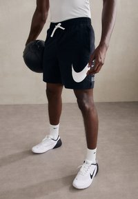 Mustat Nike-shortsit, joissa on valkoinen logo, elastinen vyötärönyöri ja musta koripallo. Yhdistetty valkoisiin lenkkarikenkiin ja sukkiin.