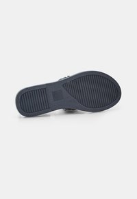 Zwarte rubberen zool met een gestructureerd oppervlak, voorzien van een geometrisch patroon en een lichte rand rondom de rand voor grip en stabiliteit.