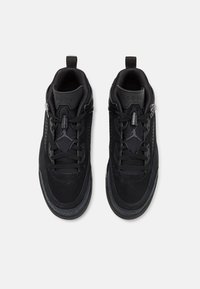 Black athletic shoes with a smooth suede upper, textured panels, rubber soles, and lace-up closure. Features branding on the tongue and side.