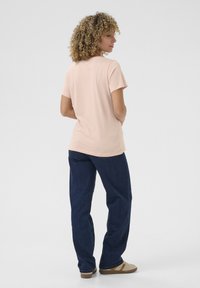 Ljusrosa t-shirt med korta ärmar i mjukt tyg, kombinerad med lösa blå denimjeans, sedd från baksidan.