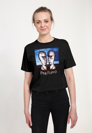 Kvinde iført en sort T-shirt med Pink Floyd albumcover, der viser to metalliske ansigter mod en blå himmelbaggrund.