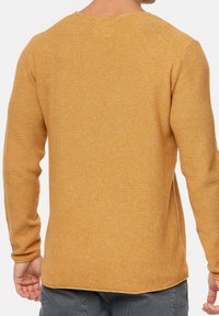 Suéter de manga larga en color mostaza con un patrón de tejido texturizado, cuello redondeado y dobladillo ligeramente curvado en los lados.