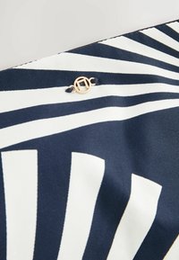 Marinblå och vit randig väska gjord av slitstarkt material, med en detaljerad rund logotyp i guldton. Ljusa ränder skapar ett iögonfallande mönster.