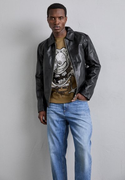 Sort jakke i imiteret læder med spids krave, parret med en brun grafisk sweater med et tegneseriekranie og lyseblå denimjeans.