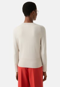 Cream knit sweater with long sleeves, ribbed detailing at the cuffs and hem, paired with bright red wide-leg trousers.