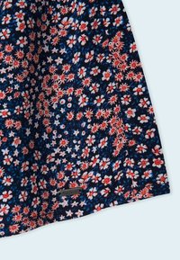 Donkerblauwe stof met een rood en wit bloemmotief en een klein rechthoekig metalen etiket met de tekst "Pepe Jeans" bij de onderrand.