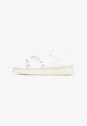 Sandalias blancas con suela plana, tiras elásticas con tachuelas plateadas, hebilla ajustable y suela texturizada para mayor agarre.