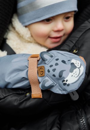Helle blaue Winterhandschuhe mit einem Cartoon-Leoparden-Gesicht, mit beige Akzenten und einem sicheren Riemen, die auf einer schwarz-creamfarbenen Jacke liegen.