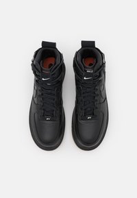 Svarta höga sneakers med överdel av texturerat läder, svarta snören, röda detaljer inuti och en framträdande logotyp på sidan och tungan.