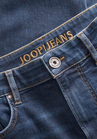 Blugi din denim albastru închis, cu broderie aurie a logo-ului „JOOP!JEANS” pe talie, nasture metalic argintiu și cusături în contrast.