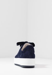 Sneaker in suede blu navy con suola bianca testurizzata e suola in gomma nera, dotato di un accento a fiocco sul tallone e foderato internamente in modo liscio.