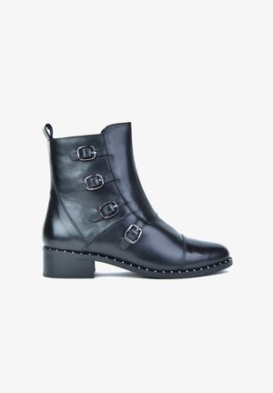 Botín negro de piel hasta el tobillo con cuatro hebillas laterales, tacón bajo tipo bloque y borde con tachuelas a lo largo de la suela, con textura suave y diseño ajustado.