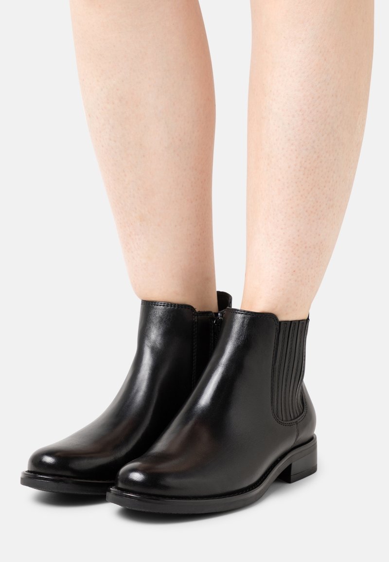 Černé kožené kotníkové boty s hladkým povrchem, bočními elastickými panely a nízkým masivním podpatkem, s kulatou špičkou a minimálními kovovými doplňky.