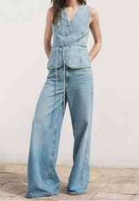 Lyseblåt denimoutfit med en ærmeløs, v-udskåret top med knapper og vidtbenede bukser med afslappet pasform og snøre i taljen.